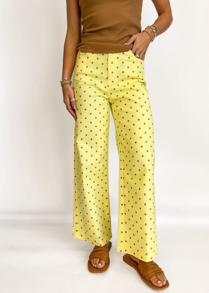 Person wearing yellow polka dot pants and brown top on a white background