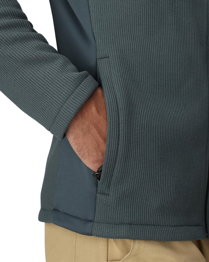 Close-up of a person wearing a dark green jacket with a zipper pocket.