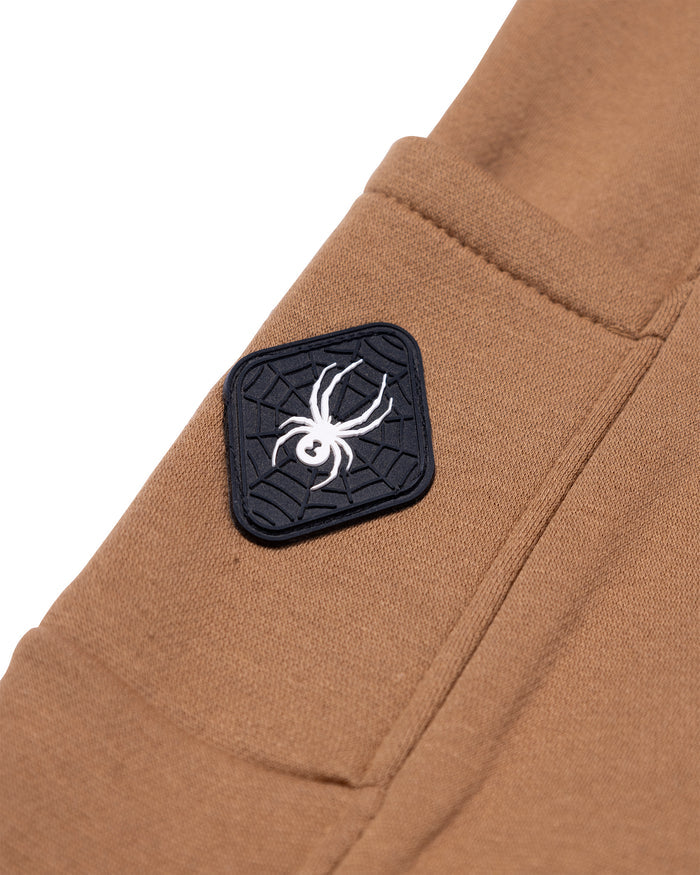 Brown pants with a spider logo patch on a white background