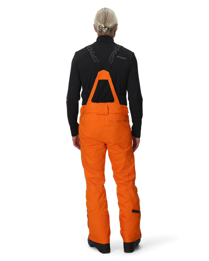 Person wearing black top and orange bib overalls on a white background