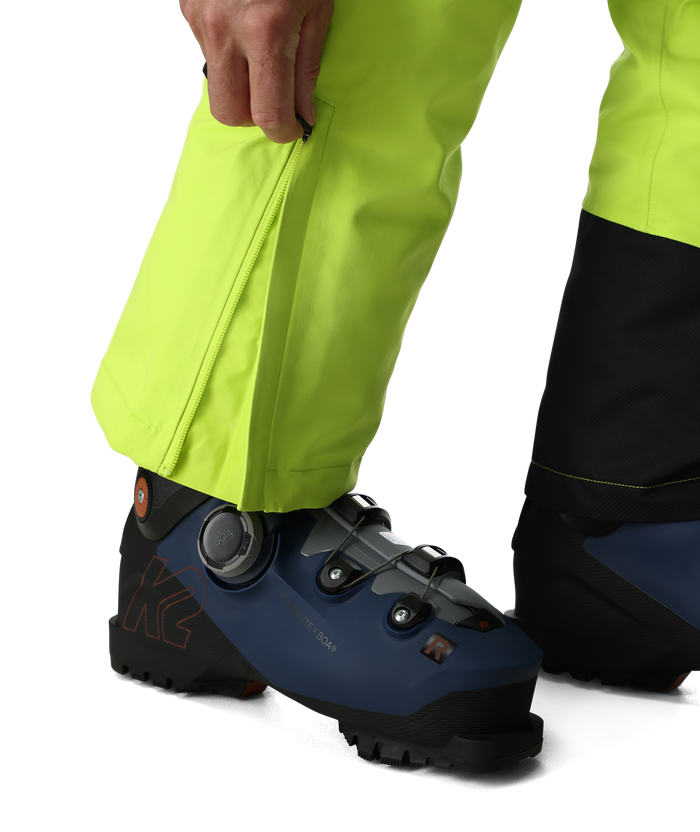Close-up of a person wearing bright yellow pants and blue ski boots on a white background