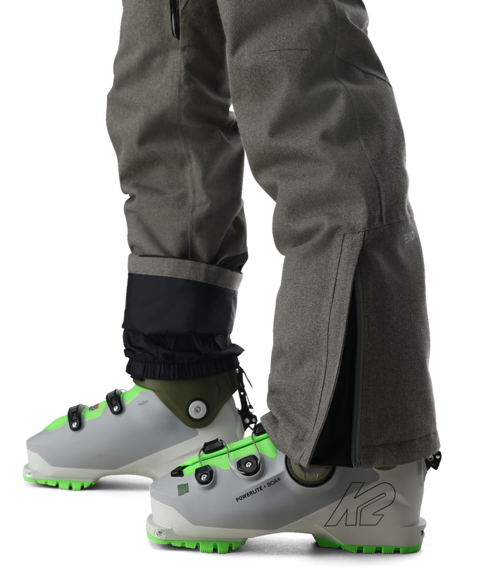 Gray ski boots with green accents worn with gray pants on a white background