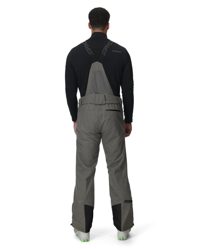 Person wearing gray bib overalls with black sleeves on a white background