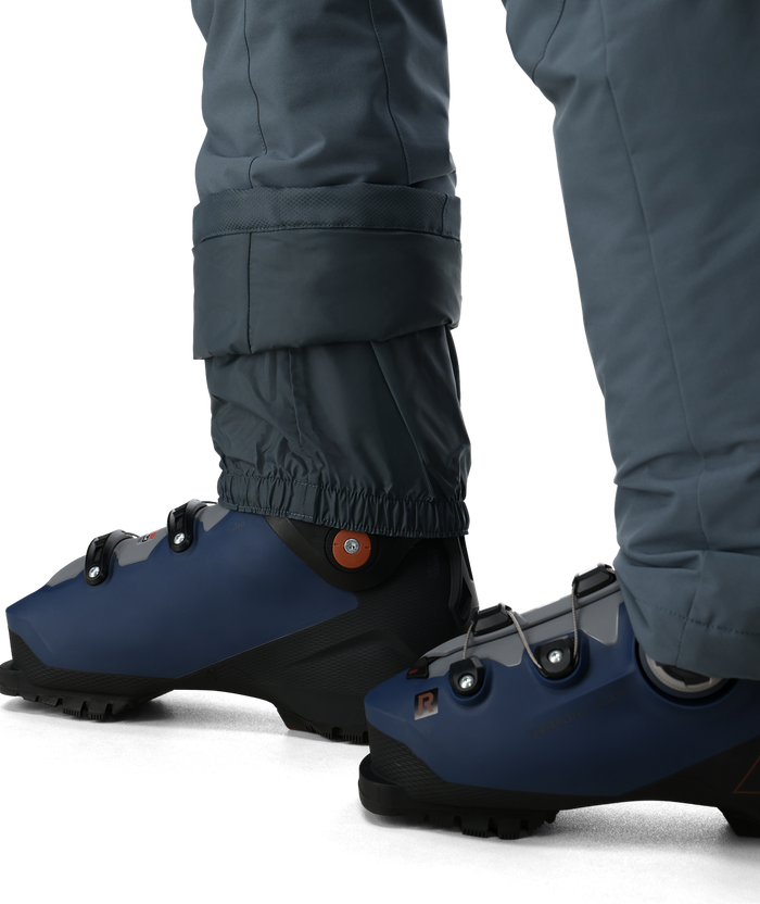 Blue slip-on shoes with black soles worn by a person in gray pants on a white background