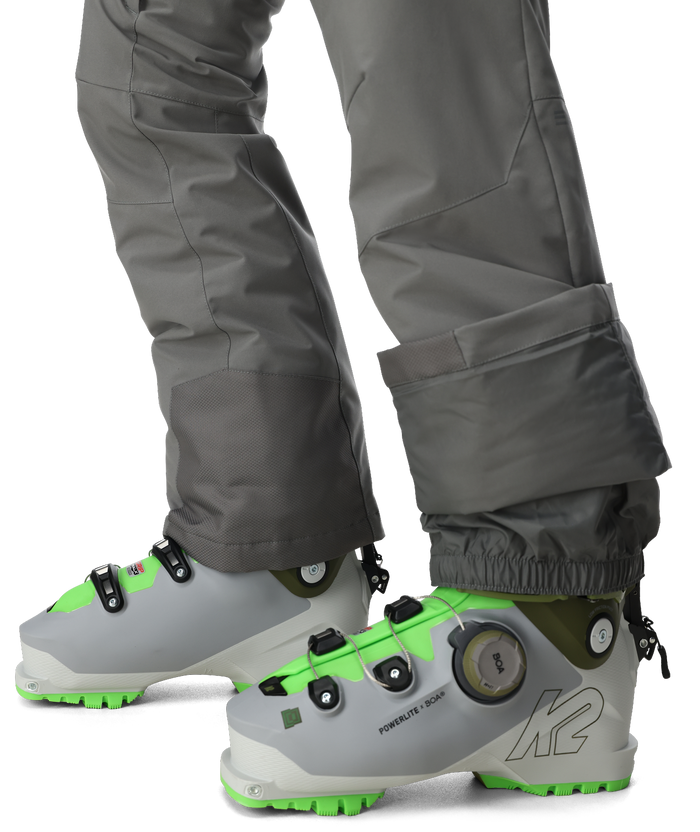 Gray ski boots with green accents worn with gray pants on a white background