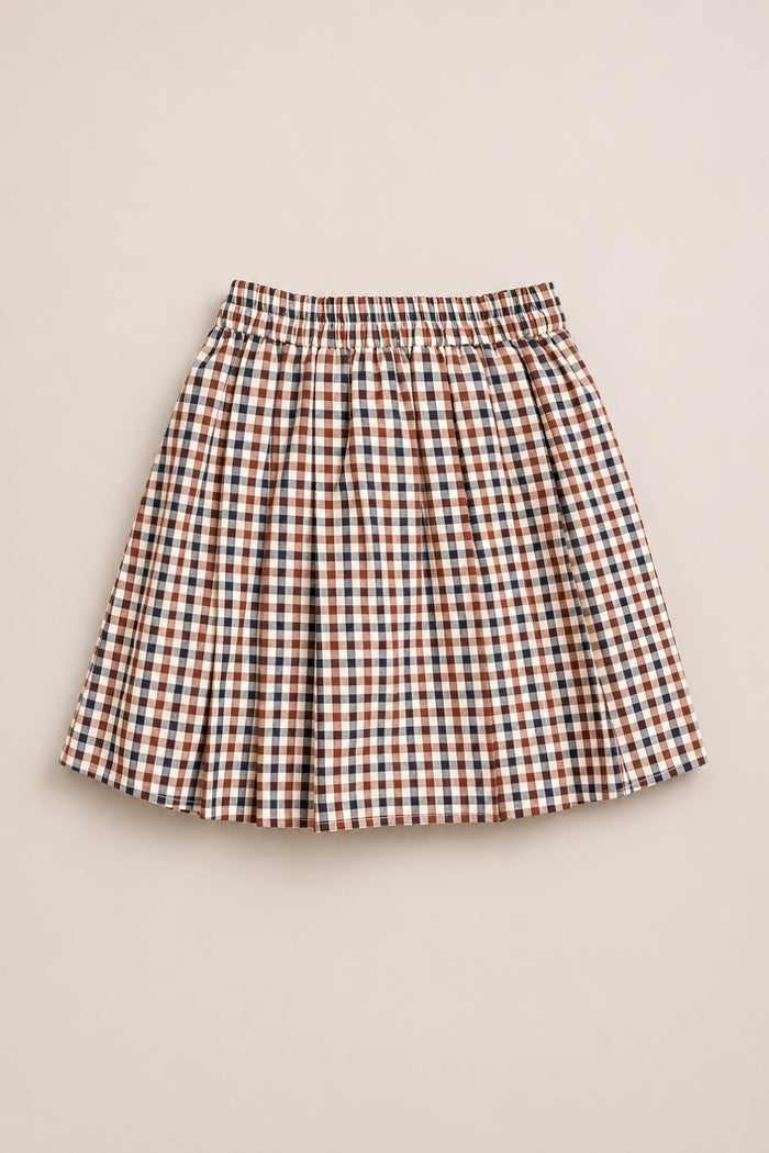 The Ivy City Co Mini Addison Skort in Chestnut Gingham features a brown, black, and white checkered pattern, pleated design, elastic waistband, and built-in shorts for added comfort. Crafted from soft cotton, it is shown on a light beige background.