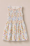 The Mini Ana Dress in Floral Fields by Ivy City Co is a sleeveless, floral print dress for girls with a smocked bodice and a bow at the neckline, shown on a light beige background.