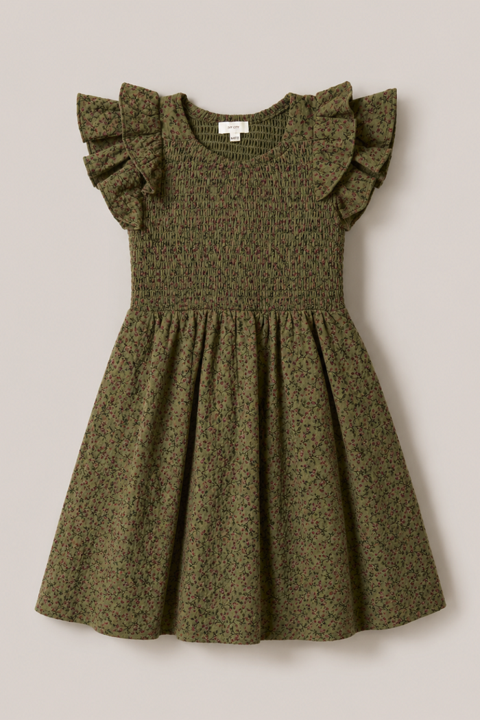 The Mini Hattie Dress in Woodland Floral by Ivy City Co is an olive green, short-sleeve cotton dress for girls showcasing a delicate small floral print, a smocked bodice, and charming ruffled sleeves. Its gathered skirt flares out beautifully. The dress is displayed laid flat on a light beige background.