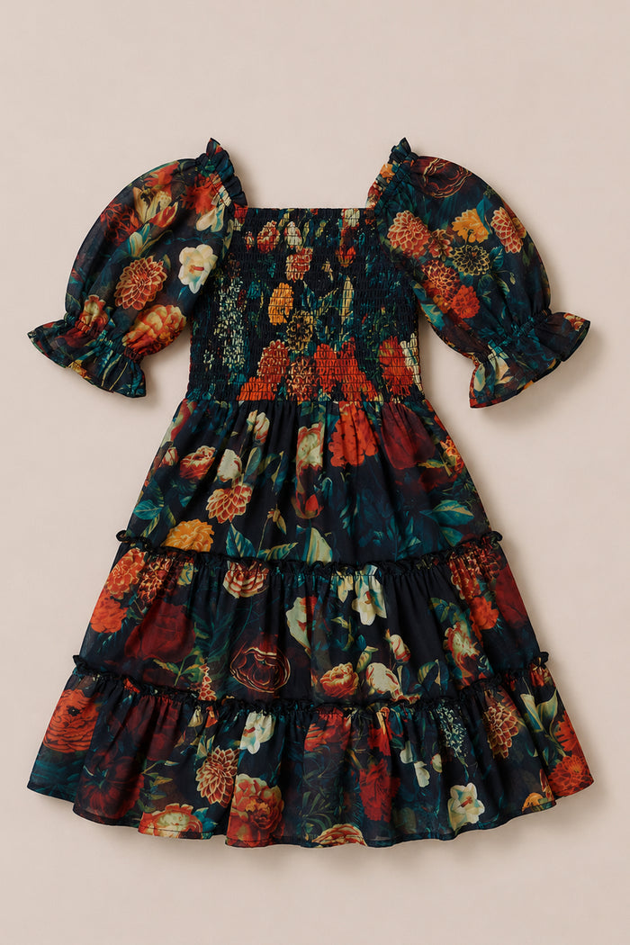 The Mini Madeline Dress in Imogen Moody Floral by Ivy City Co is a short, dark chiffon dress adorned with red, orange, and yellow flowers on a black background. It features puffed sleeves, a smocked bodice, and a tiered ruffle skirt—making it the perfect fall staple or a charming addition to your seasonal wardrobe.