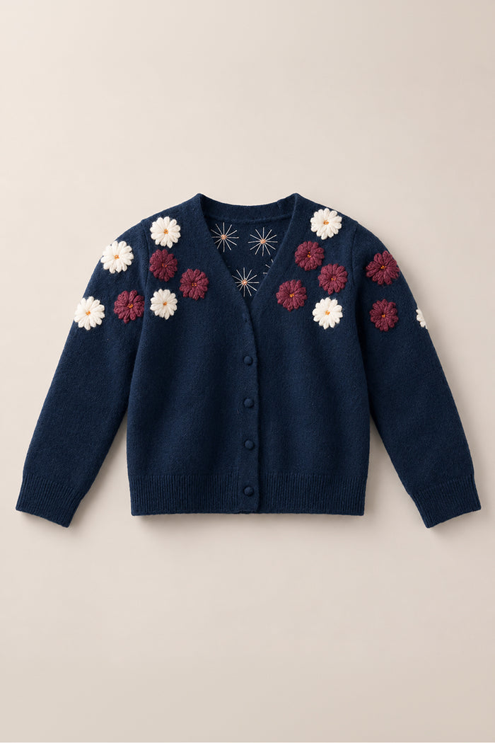 The Mini Pauline Sweater in Midnight Floral by Ivy City Co features long sleeves, a button front, and decorative white and burgundy floral appliqués adorning the shoulders and upper chest, capturing the charm of an embroidered navy blue cardigan.