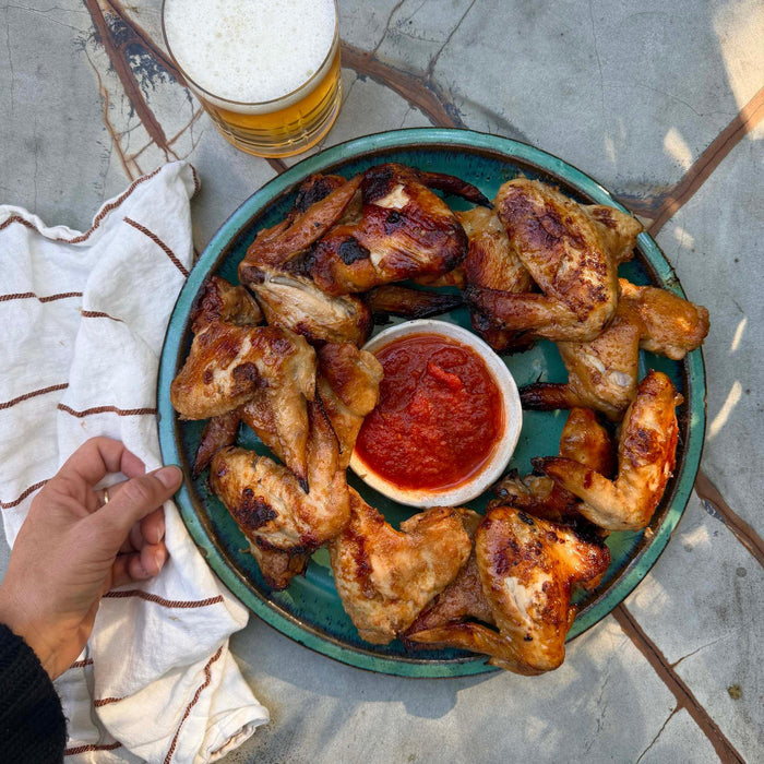 Grilled chicken wings with red sauce on a plate, paired with beer on outdoor stone table