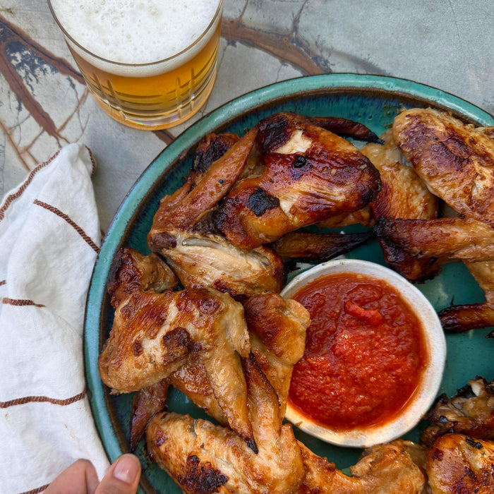 Grilled chicken wings with red dipping sauce and beer, served on a green plate