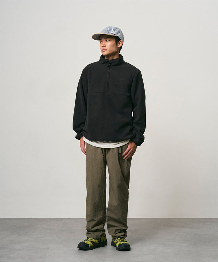Model wearing burnt olive colored Nylon Gramicci Pants and a black jacket on a light-tone background.