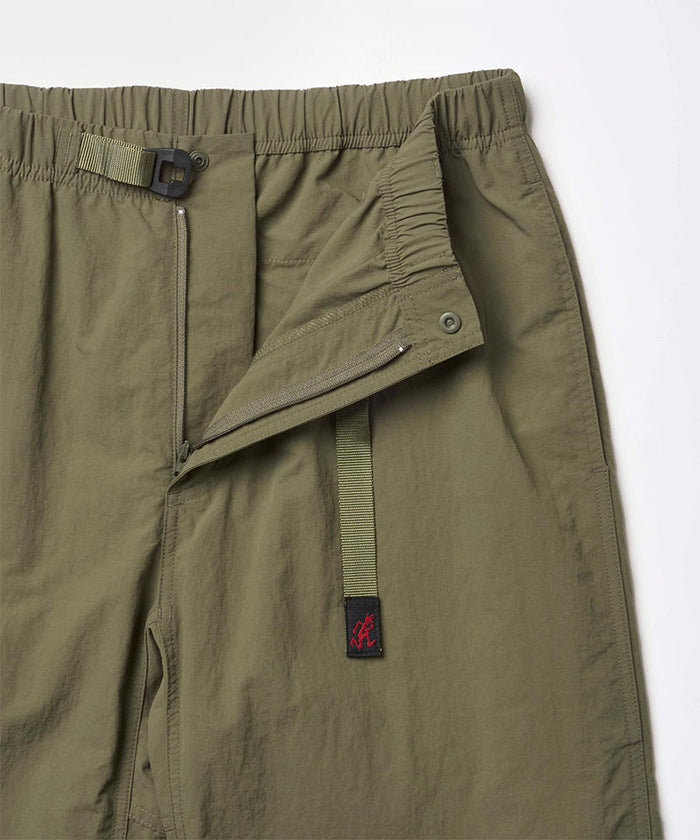 Close-up view of burnt olive colored Nylon Gramicci Pants showing waistband and zipper detail on a light-tone background.