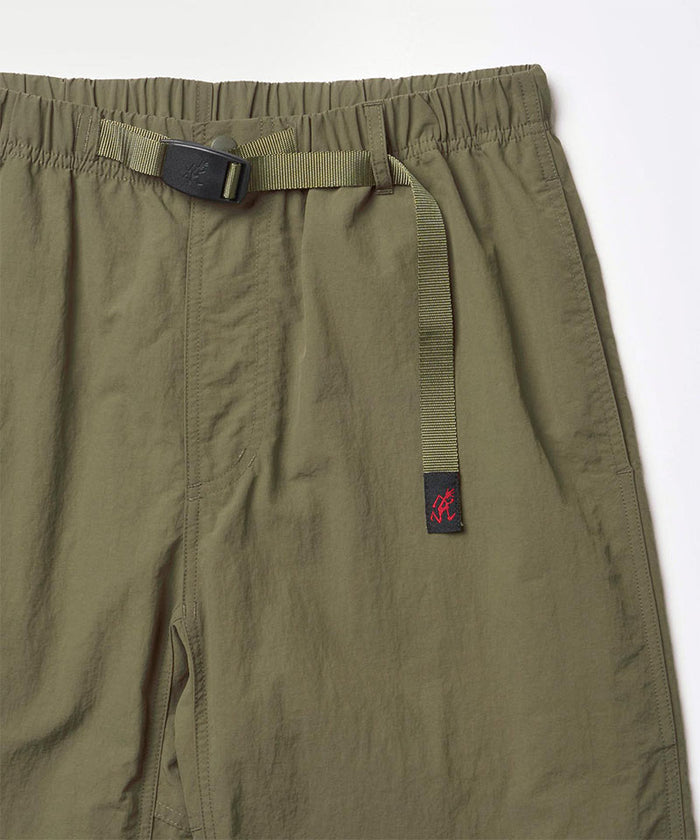 Close-up view of burnt olive colored Nylon Gramicci Pants on a light-tone background.