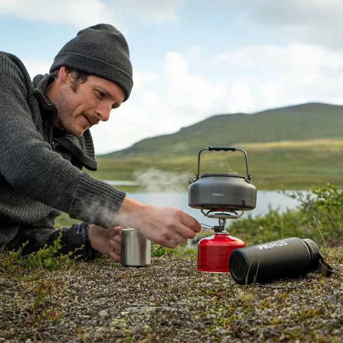 Person using a Primus Essential Trail Camping Gas Stove to boil water using a Litech kettle in a scenic outdoor setting