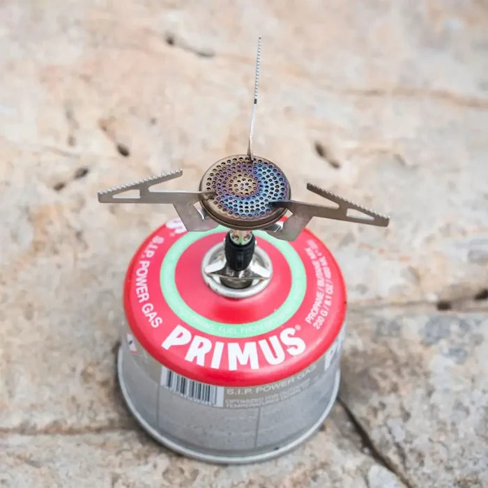 Lifestyle image of a Primus Express camping gas stove attached to a gas canister whilst standing on a rock