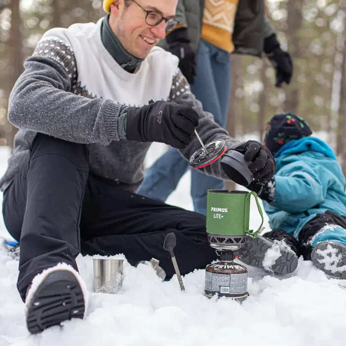 Person using a Primus Lite Plus stove in the snow with another person in the background.