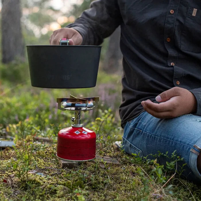 Person using a Primus Mimer Camping Gas Stove with a large cooking pot outdoors in a forest setting