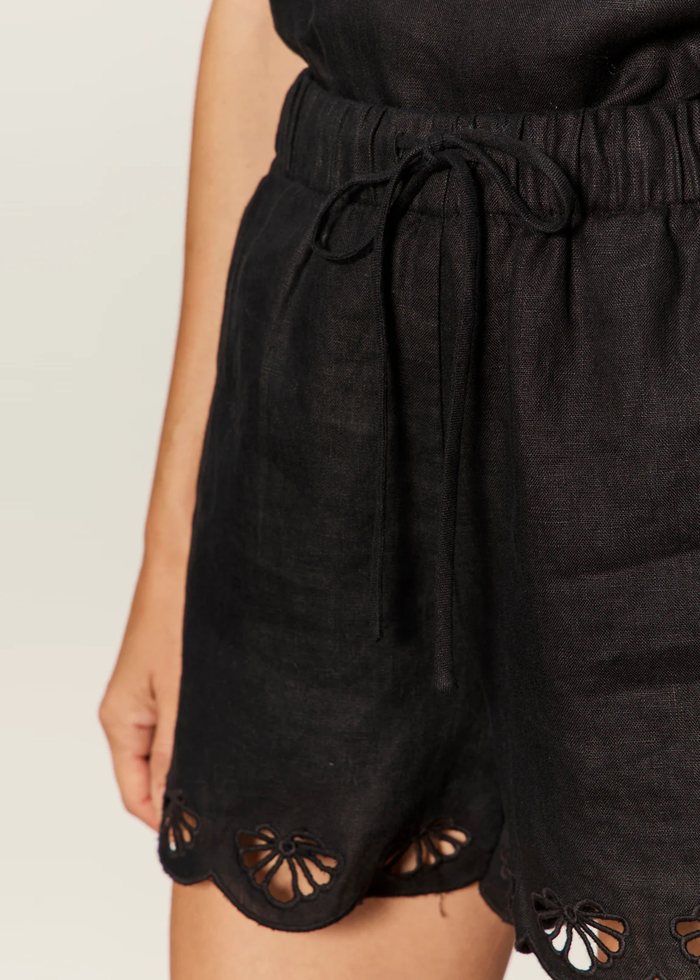 Close up of a woman wearing black linen shorts with a scalloped hem and a matching top