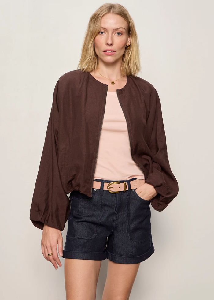 Woman wearing a brown linen jacket with a cream tank and dark blue shorts