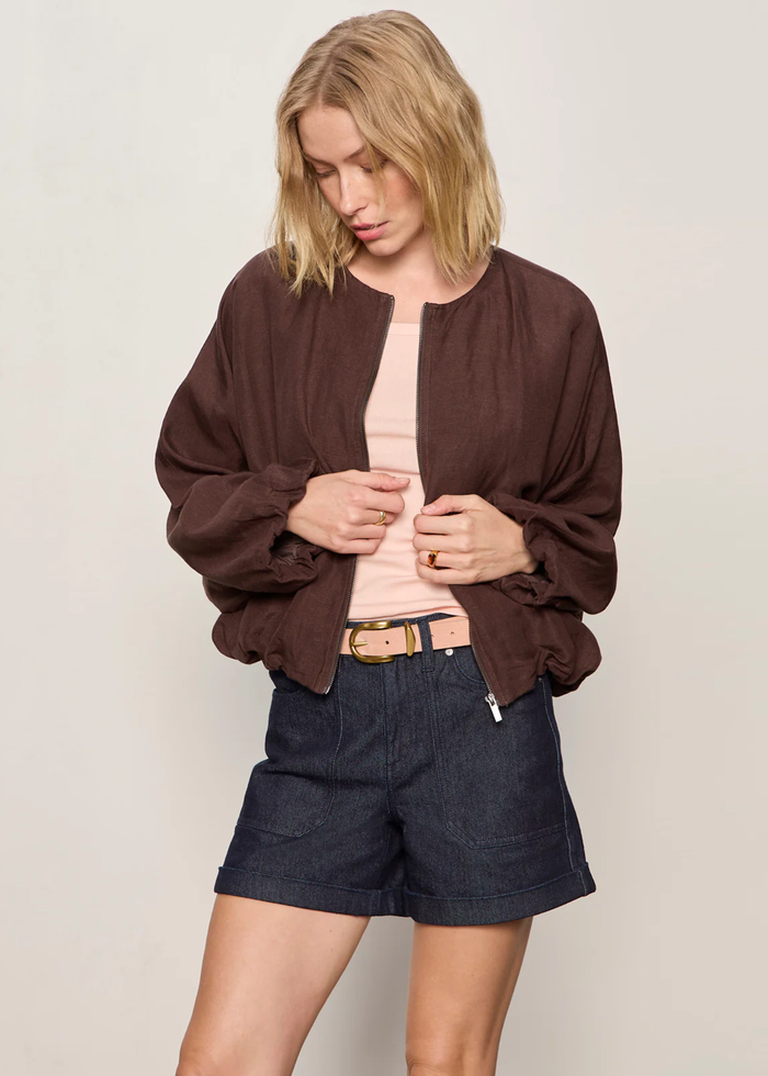 Woman wearing a brown linen jacket with a cream tank and dark blue shorts