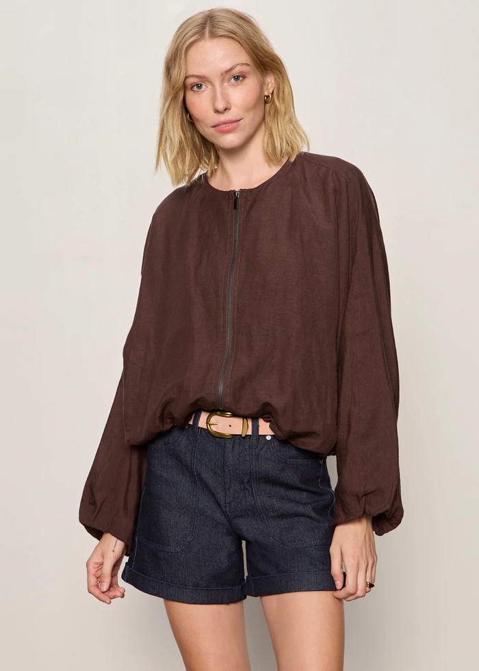 Woman wearing a brown linen jacket with a cream tank and dark blue shorts