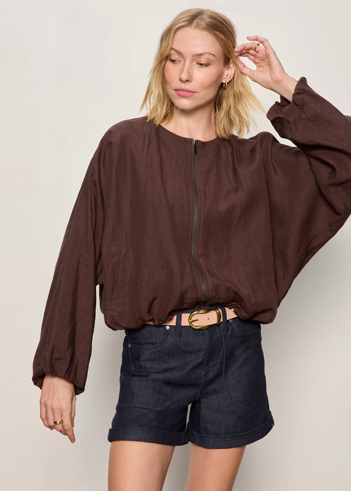 Woman wearing a brown linen jacket with a cream tank and dark blue shorts