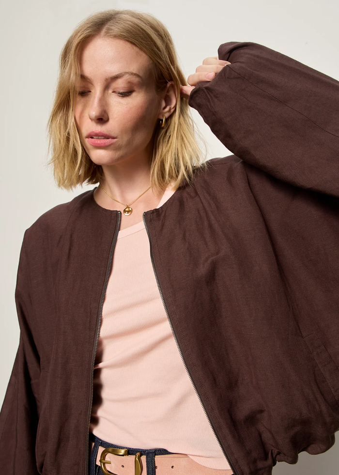 Woman wearing a brown linen jacket with a cream tank and dark blue shorts
