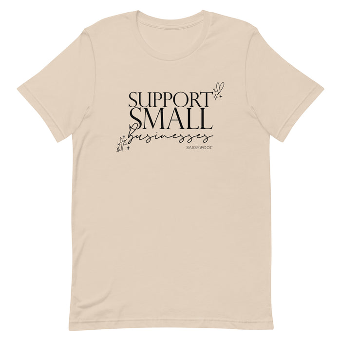 The Sassy Woof Support Small Businesses Tee is a beige unisex shirt featuring "Support Small Businesses" in black decorative text with star and heart doodles. Perfect for daily wear to show your local love!.