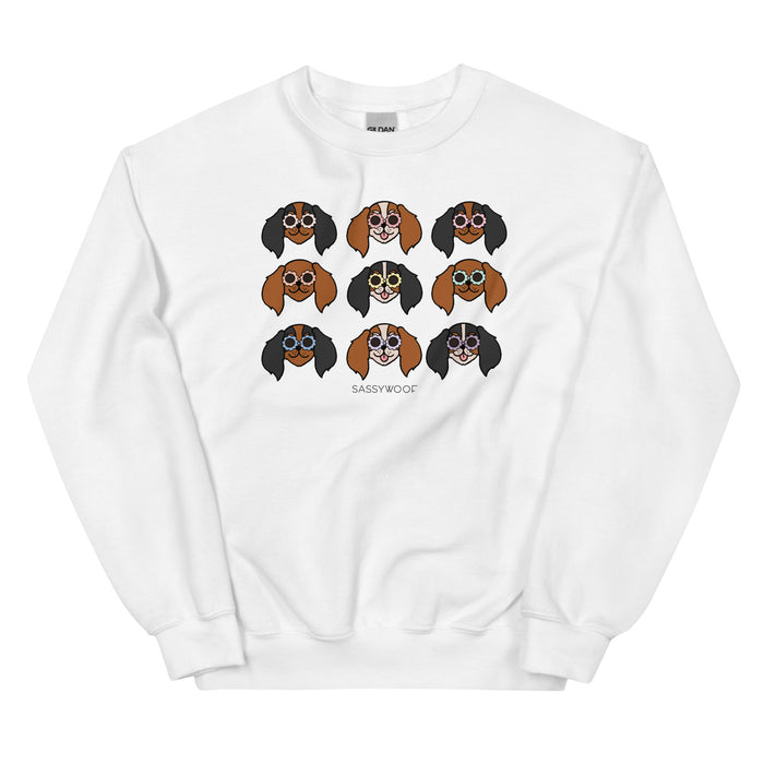 The Sassy Woof Sweatshirt - Cavaliers is a white unisex sweatshirt with a 3x3 grid of cartoon Cavalier dog faces and "SASSY WOOF" printed below—perfect playful apparel for Cavalier lovers.