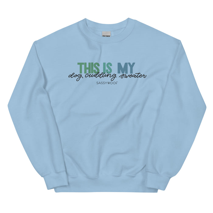 The Sassy Woof "This is My Dog Cuddling Sweater" is a light blue unisex crewneck sweatshirt featuring the phrase in green, blue, and black fonts on the front.