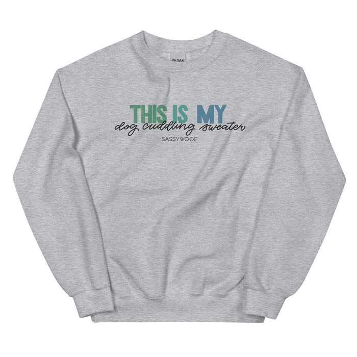 The Sassy Woof “This is My Dog Cuddling Sweater” is a light gray unisex crewneck sweatshirt featuring the phrase in teal, navy, and black fonts on the front.