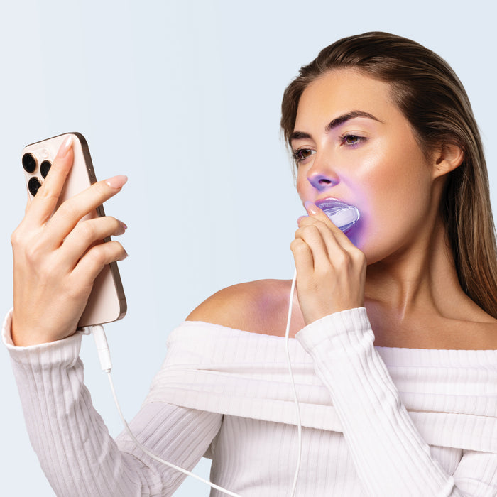 Woman holding LED teeth whitening light that connects to smartphone