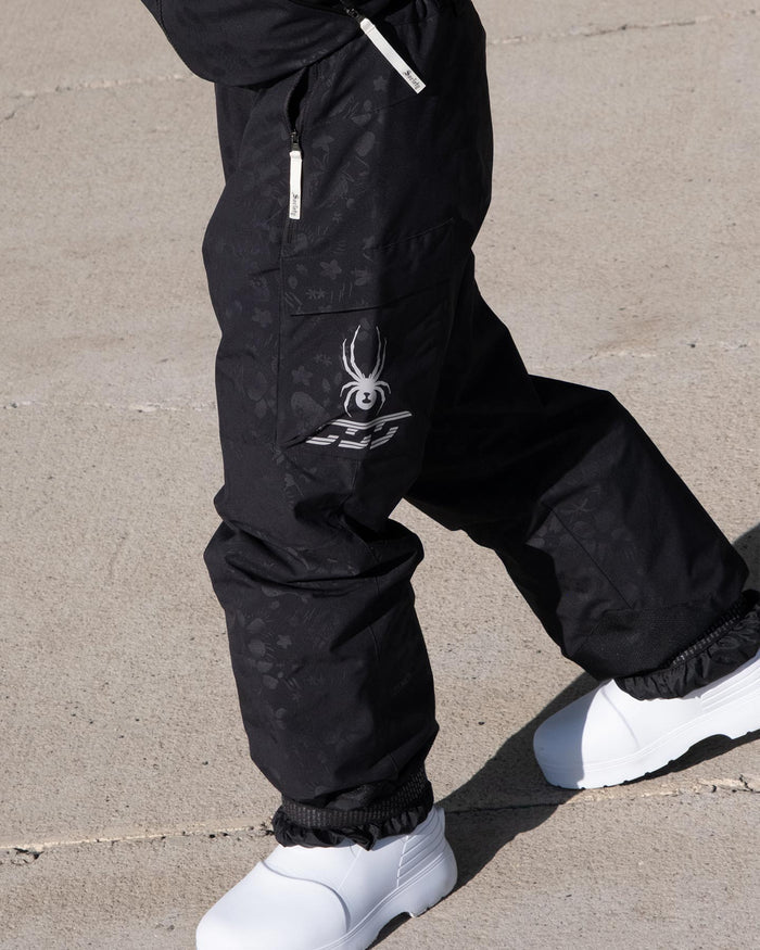 Black snow pants with a spider logo worn by a person on a concrete surface