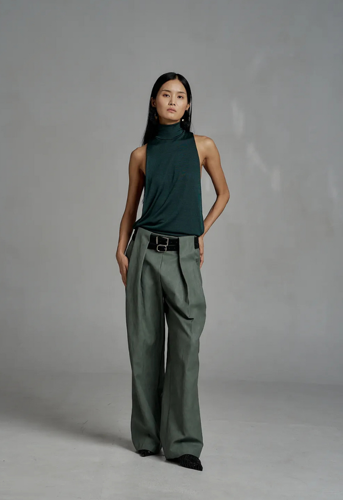 Person wearing a green sleeveless top and wide-leg pants against a gray background