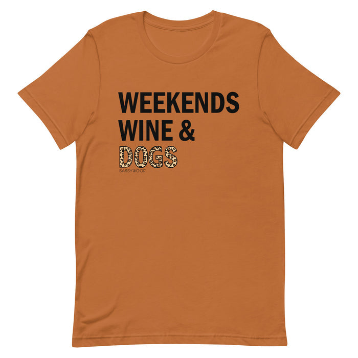 The Weekends, Wine, & Dogs Tee by Sassy Woof is an orange unisex shirt made from 100% ring-spun cotton, featuring "WEEKENDS WINE & DOGS" with "DOGS" in leopard print and a small Sassy Woof logo below. Perfect for wine and dog lovers!.