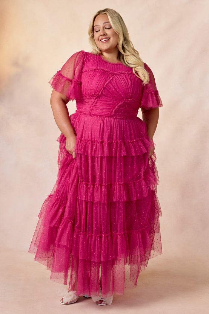 A woman with long blonde hair stands smiling with her eyes closed against a beige background, wearing the Whimsical Dress in Fuchsia by Ivy City Co—featuring tiered ruffle tulle skirt, sheer sleeves, polka dot details, and dress pockets.